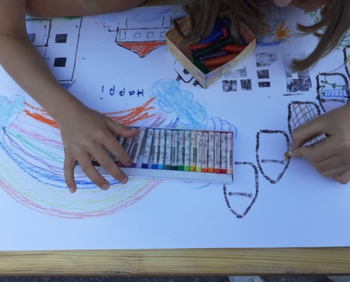 Kinder malen eine Stadt mit Häusern, Wolken und Regenbogen. Auf dem Bild steht "Happi" - gemeint ist das englische "happy" = glücklich