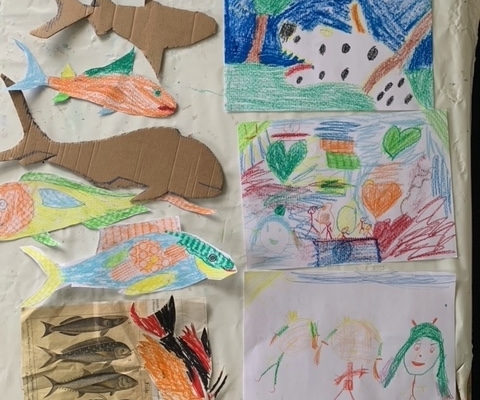 Rechts sind drei bunte Kinderbilder mit einem Hund mit schwarzen Punkten, Herzen und Kindern übereinander angeordnet. Auf der linken Seite sind Fische, ein Hai und ein Delfin aus Papier bzw. Pappe aufgeklebt.