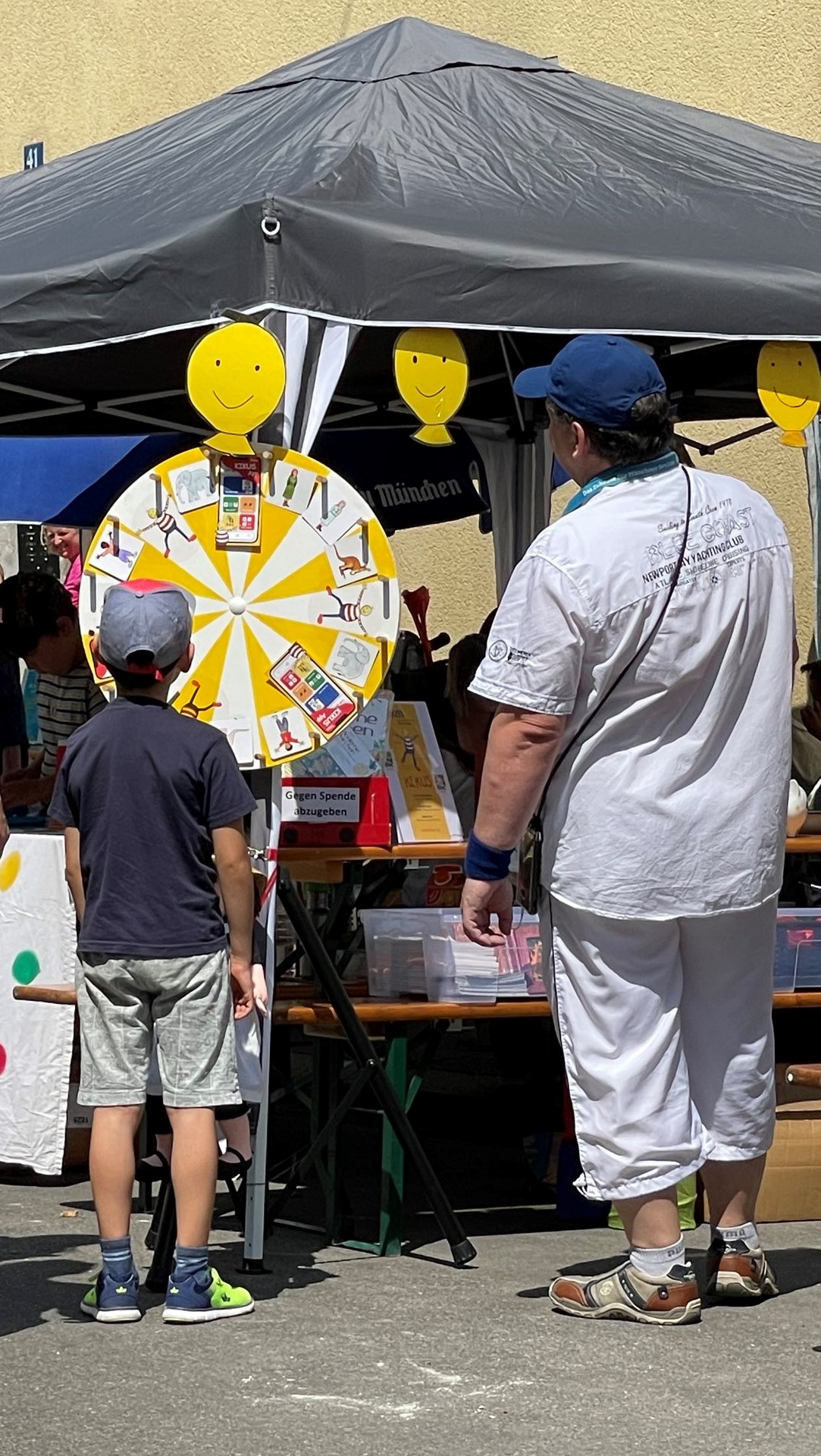 Kind Mann vor einem Glücksrad an buntem Stand